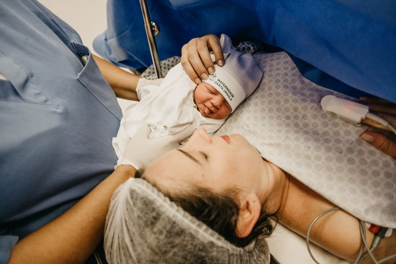 hero-img-01 A mother cradling her newborn immediately after childbirth in a hospital setting.