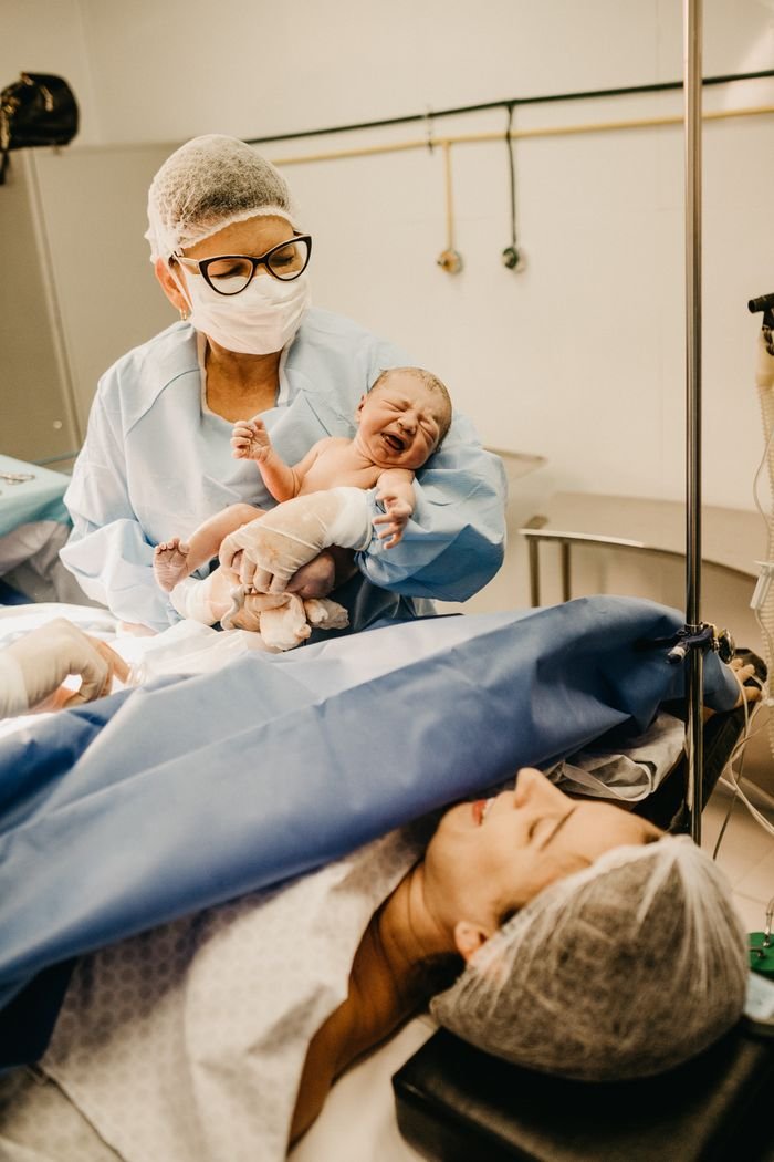 our-services-1 A doctor holds a newborn baby in a hospital setting post-delivery.