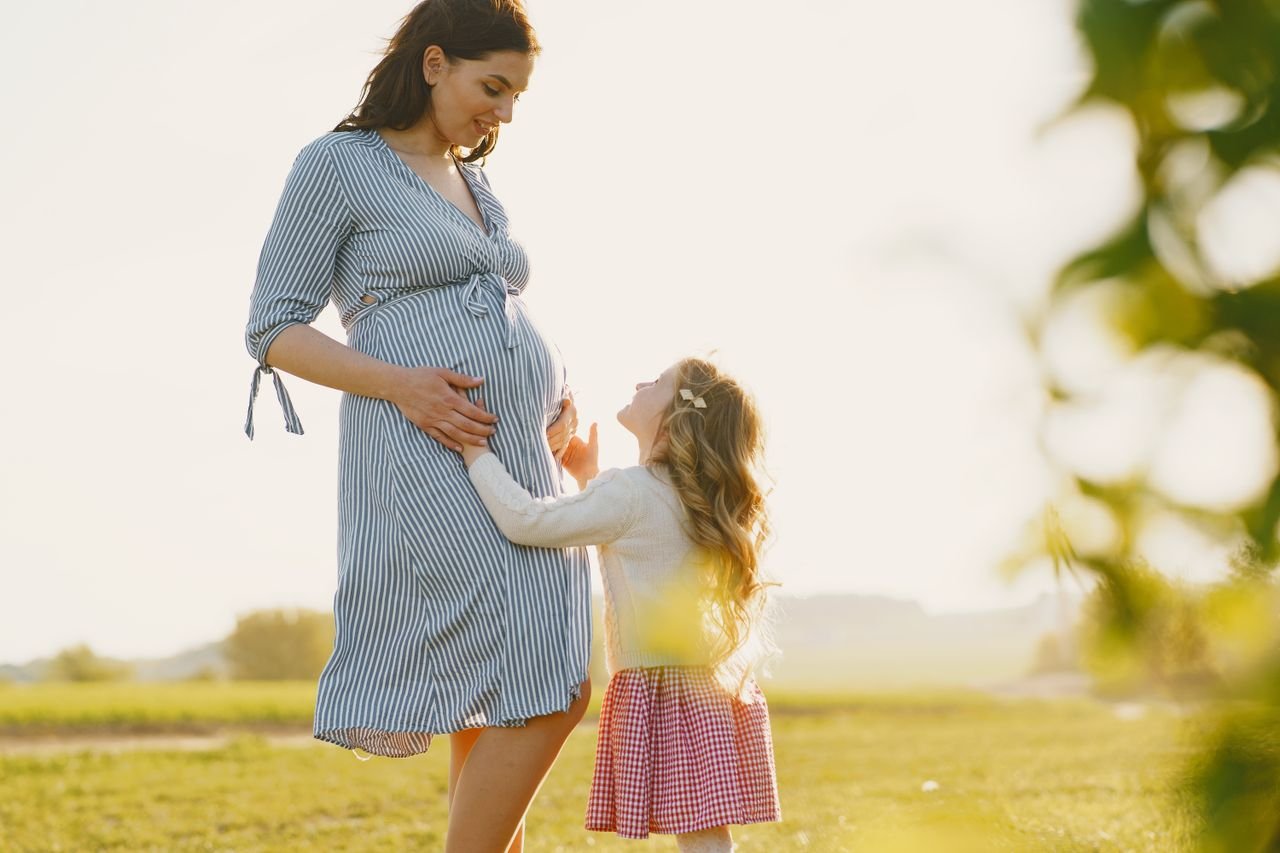 hero-img-02 Heartwarming scene of a pregnant mother and her daughter bonding in a sunlit field.