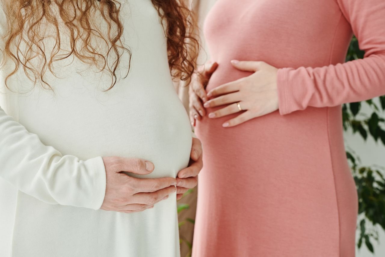 about-01 Two expectant women gently holding their pregnant bellies, symbolizing motherhood and maternity.